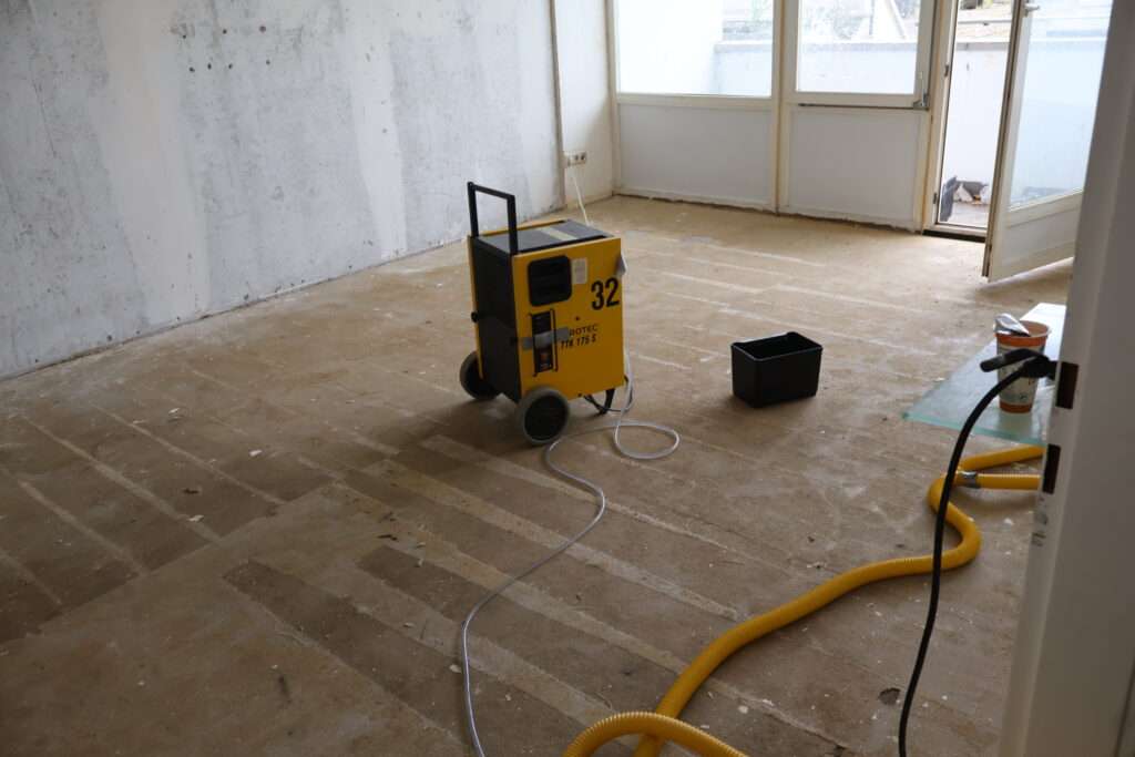 Wasserschadensanierung – Bautrockner im Einsatz zur Feuchtigkeitsreduzierung nach einem Wasserschaden in einem Wohnraum.